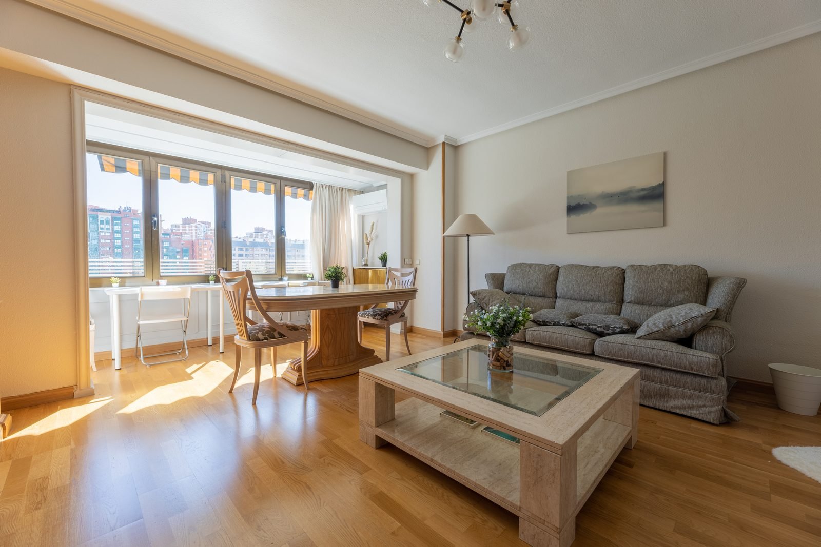 Salón luminoso de una vivienda gestionada por Verantia, con ventanal, sofá, mesa de comedor y suelo de madera